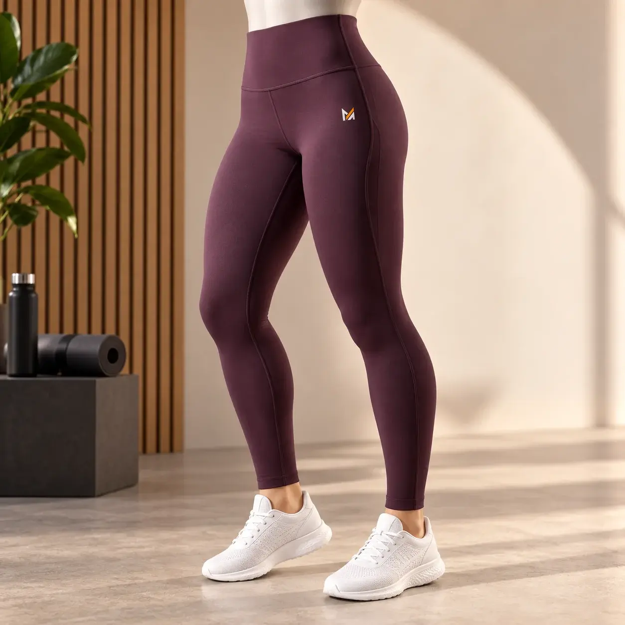 High-waisted burgundy performance leggings displayed on a mannequin with a small Mega Apparel logo in a modern fitness studio setting.